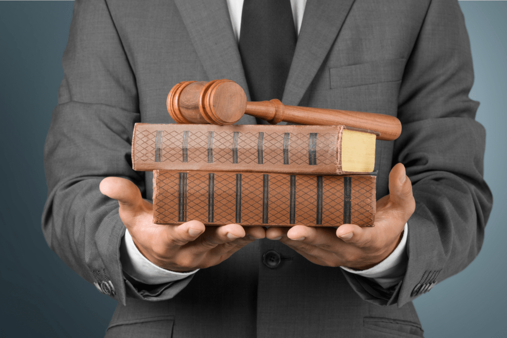 A person in a suit holds two stacked legal books with a wooden judge's gavel resting on top, symbolizing the importance of regulatory changes and beneficial ownership in today's legal landscape.