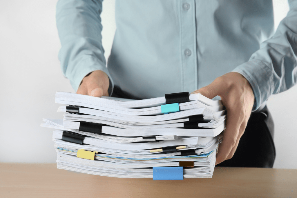A person holds a large stack of paper documents organized with various colored binder clips, illustrating best practices for SMBs, resting on a desk.